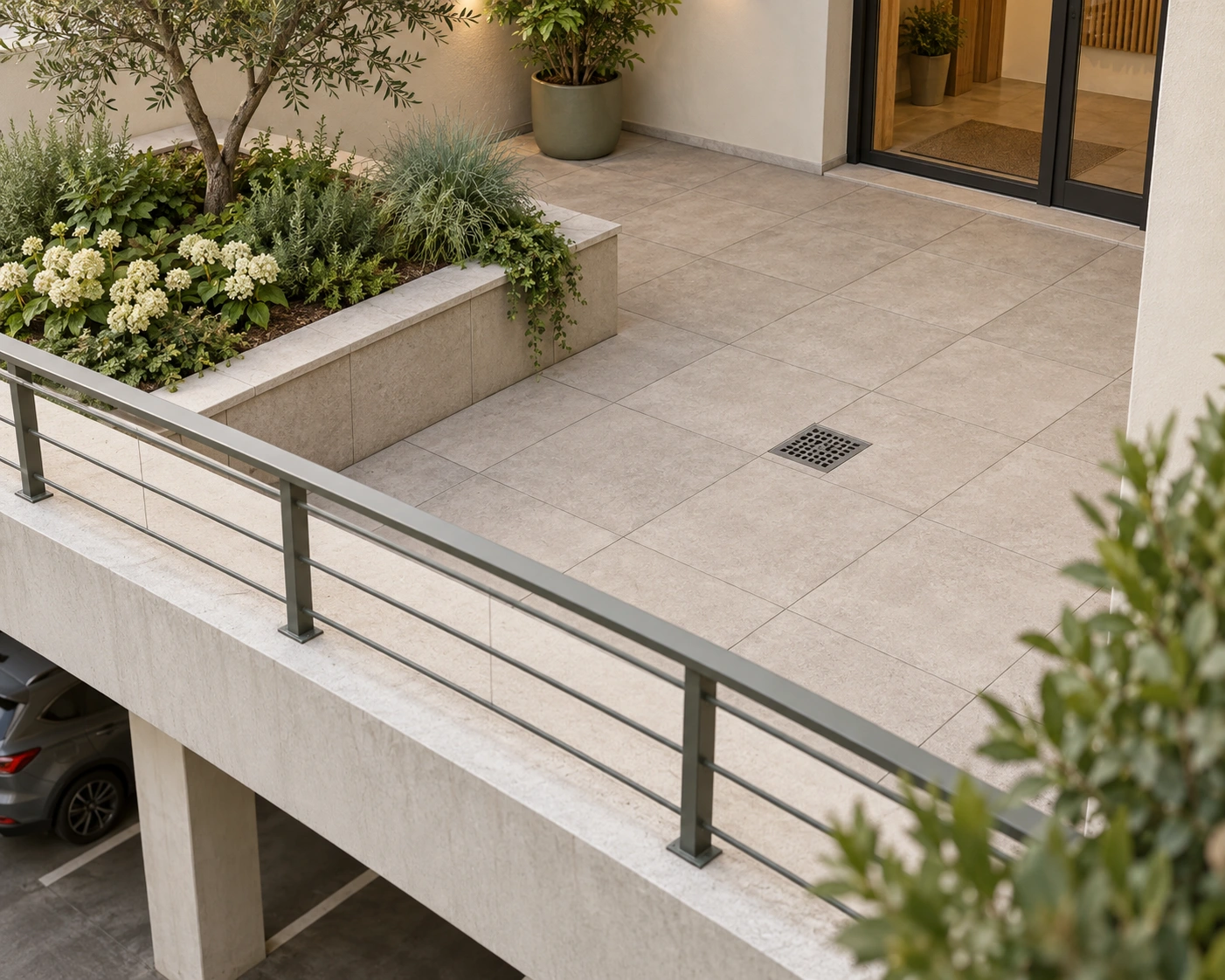 Courtyard paving, planter, metal surface grate and doorway visible; layers and drain route concealed, no slope or capacity proved.